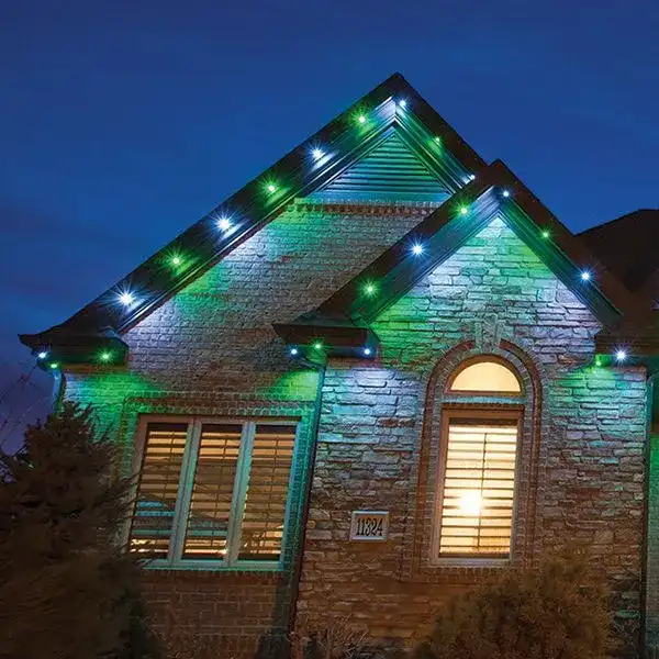 Brick home at dusk with green and white permanent lighting along the gables